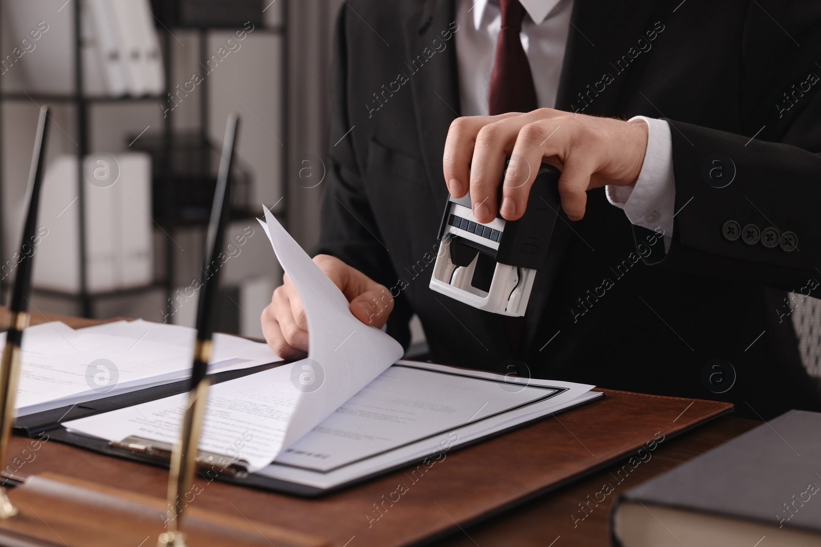 Photo of Notary stamping document at table in office, closeup