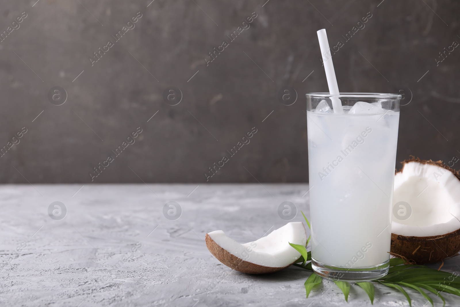 Photo of Glass of coconut water with ice cubes, palm leaf and nut on grey table. Space for text