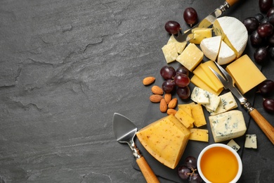 Photo of Cheese platter with specialized knives and fork on dark table, top view. Space for text