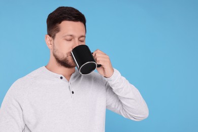 Photo of Man drinking from black mug on light blue background. Space for text