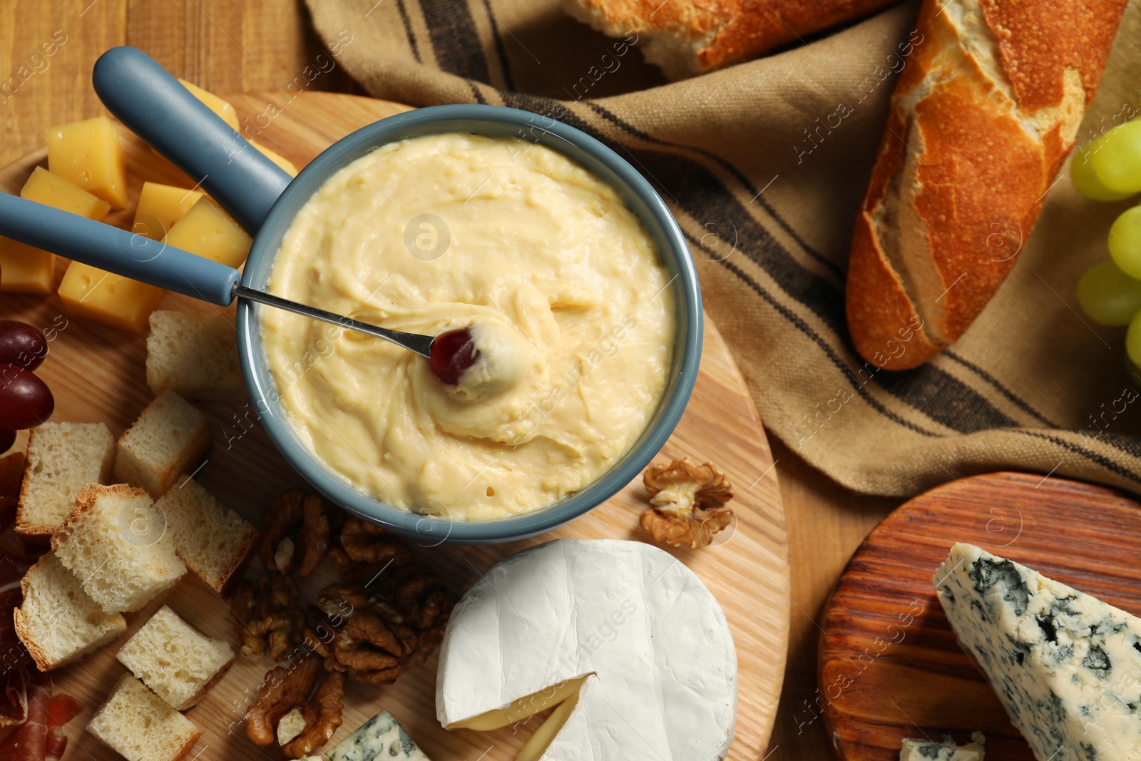 Photo of Fondue pot with tasty melted cheese, fork and different snacks on wooden table, top view