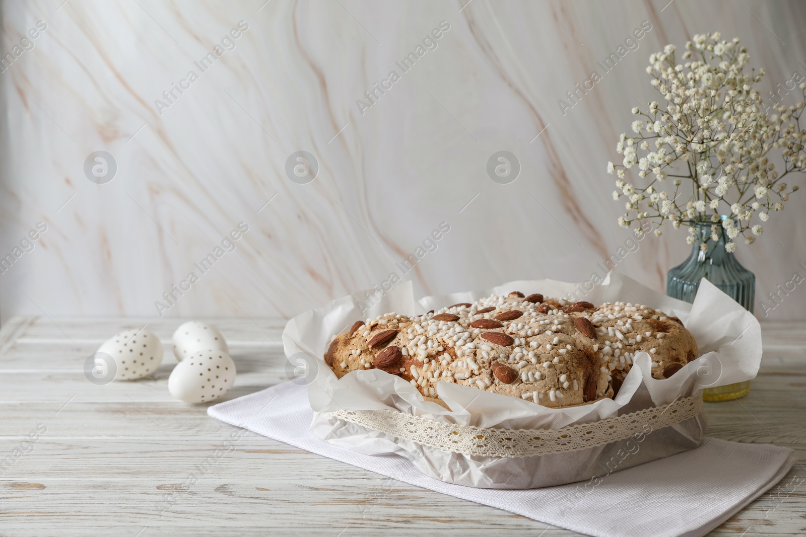 Photo of Delicious Italian Easter dove cake (traditional Colomba di Pasqua), decorated eggs and flowers on white wooden table. Space for text