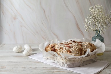 Delicious Italian Easter dove cake (traditional Colomba di Pasqua), decorated eggs and flowers on white wooden table. Space for text