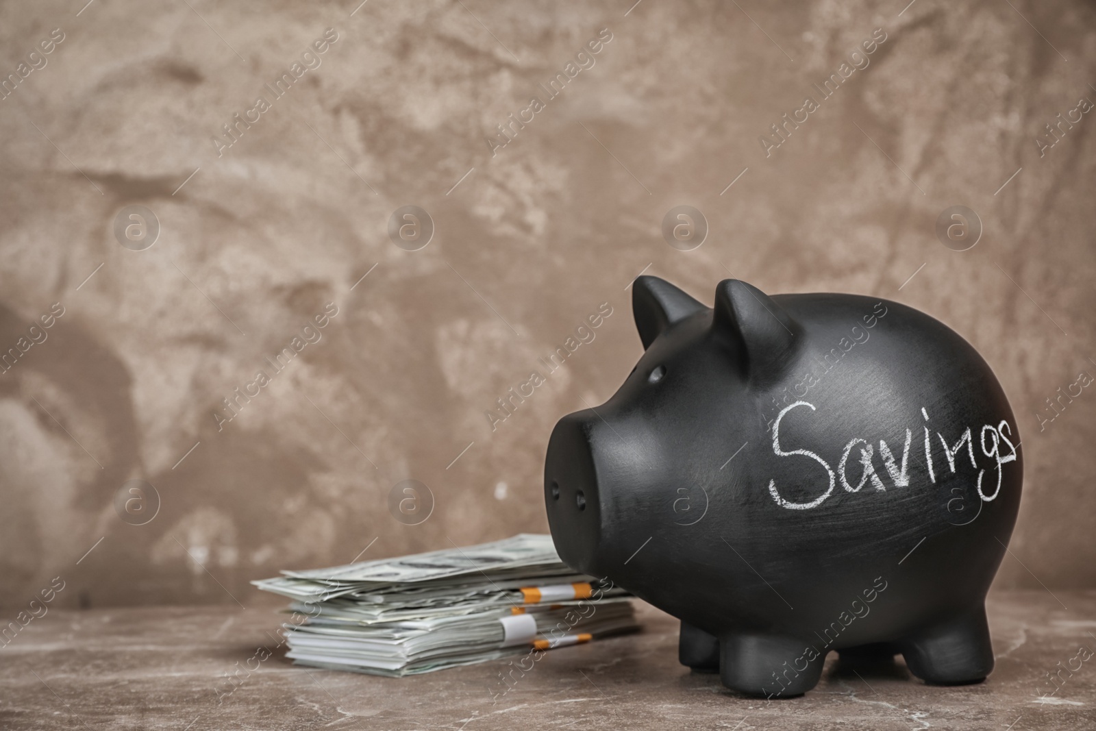 Photo of Black piggy bank with word SAVINGS and money on table