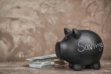 Photo of Black piggy bank with word SAVINGS and money on table