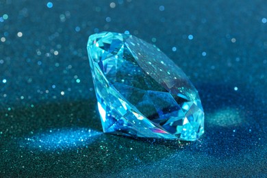 Photo of Beautiful dazzling diamond on light blue glitter background, closeup