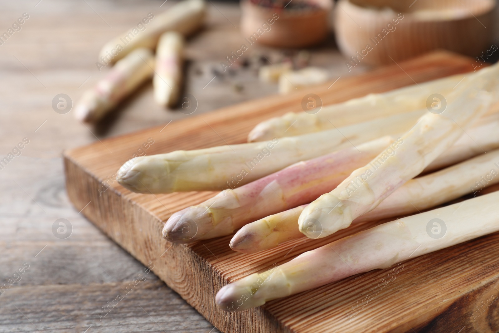 Photo of Fresh white asparagus and cutting board on wooden table, closeup