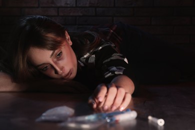 Photo of Addicted woman near different drugs on floor