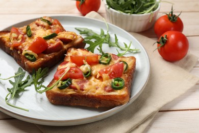 Tasty pizza toasts, fresh tomatoes and arugula on light wooden table, closeup