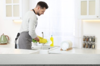 Image of Man doing washing up in kitchen, focus on empty grey stone table