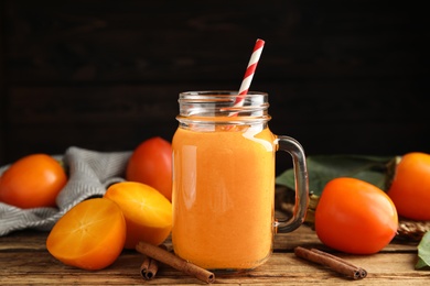 Tasty persimmon smoothie with straw and fresh fruits on wooden table