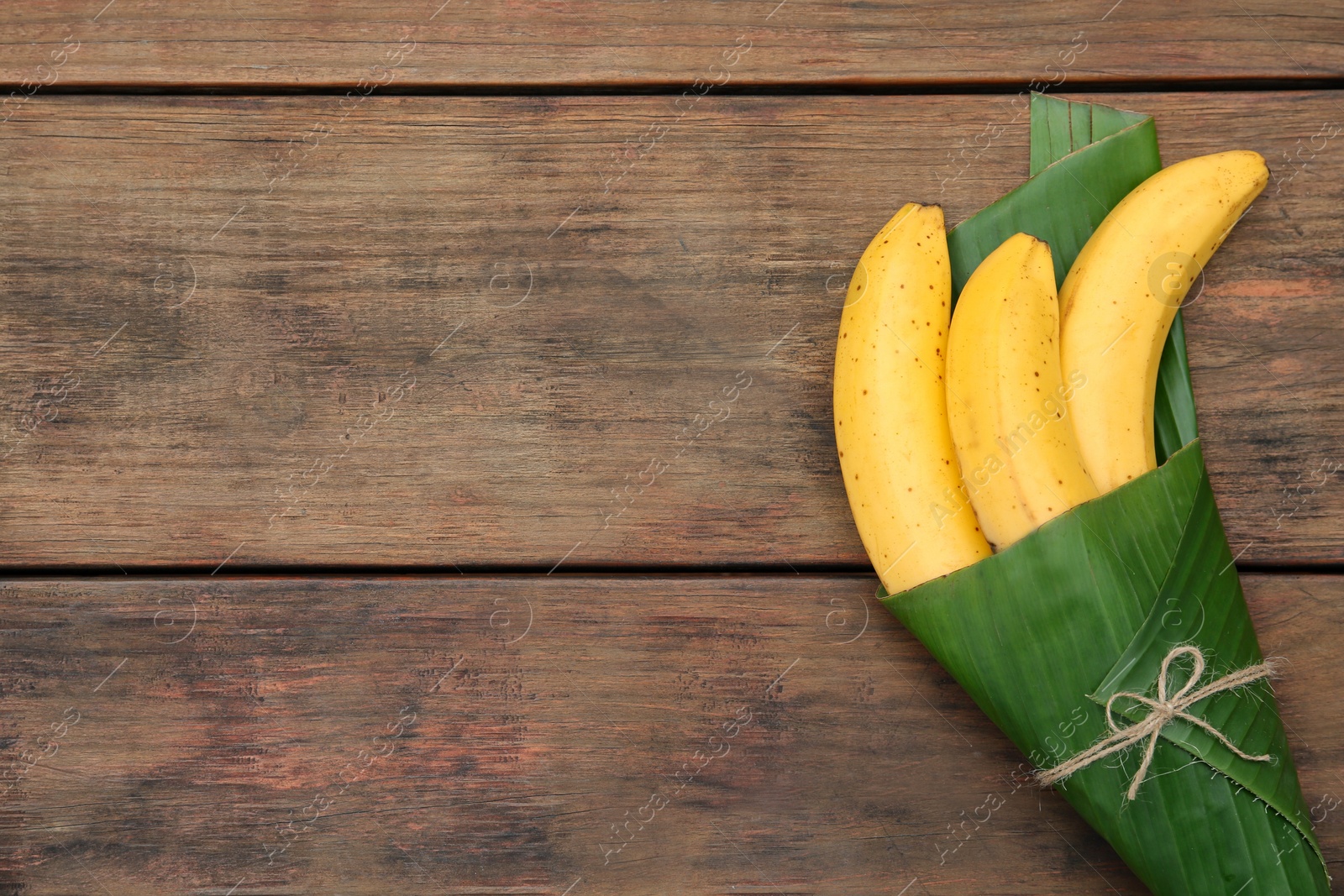 Photo of Delicious ripe bananas wrapped in fresh leaf on wooden table, top view. Space for text