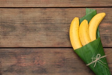 Photo of Delicious ripe bananas wrapped in fresh leaf on wooden table, top view. Space for text