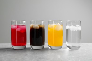 Photo of Glasses of different refreshing soda water with ice cubes on light grey marble table