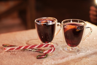 Photo of Glass cups of mulled wine and candy canes on table covered with snow outdoors. Space for text