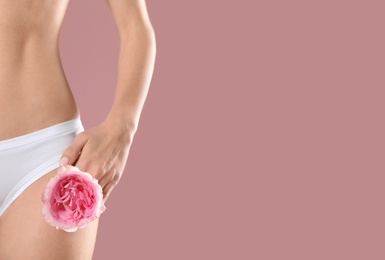 Young woman with flower showing smooth silky skin after epilation on color background