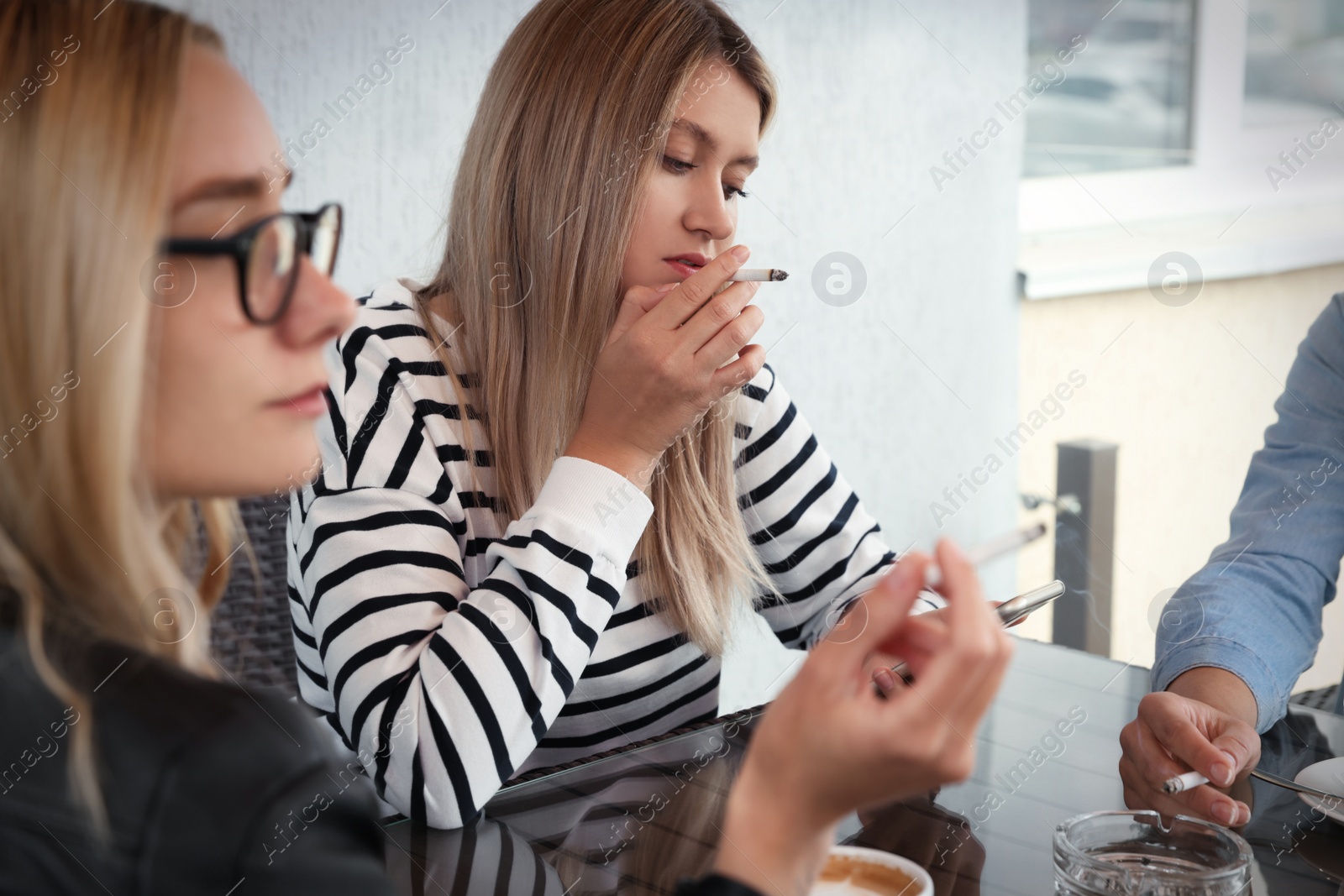 Photo of Women smoking cigarette at table in outdoor cafe