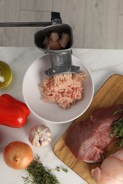 Metal meat grinder with chicken mince and products on white marble table, flat lay