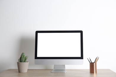 Photo of Modern computer monitor on table against white wall. Mock up with space for text