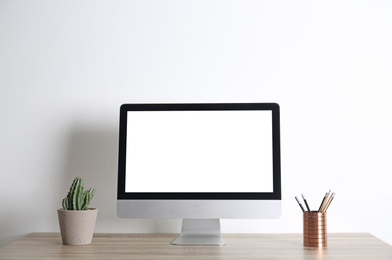 Modern computer monitor on table against white wall. Mock up with space for text