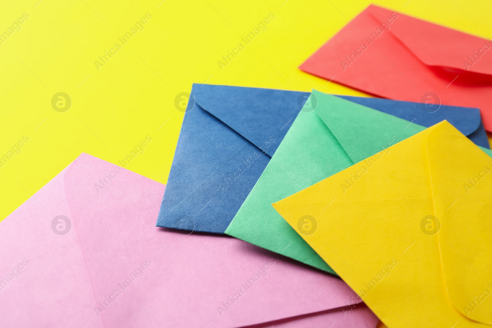 Photo of Colorful paper envelopes on yellow background, closeup