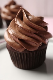 Delicious chocolate cupcake with cream on plate, closeup