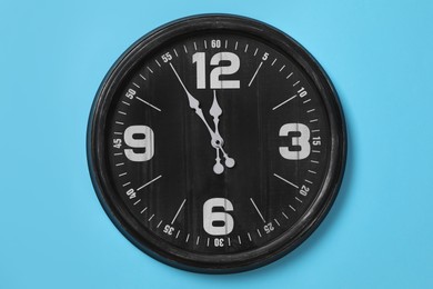 Stylish analog clock hanging on light blue wall. New Year countdown