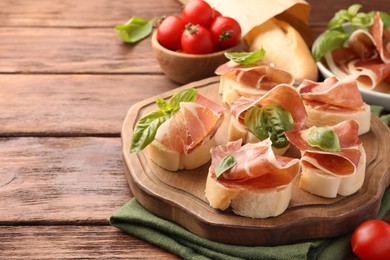 Photo of Tasty sandwiches with cured ham, basil leaves and tomatoes on wooden table. Space for text