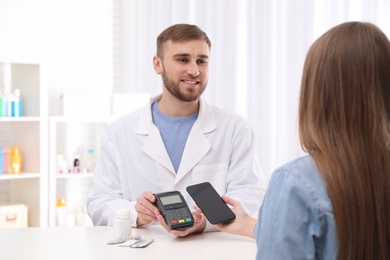 Woman using terminal for contactless payment with smartphone in pharmacy