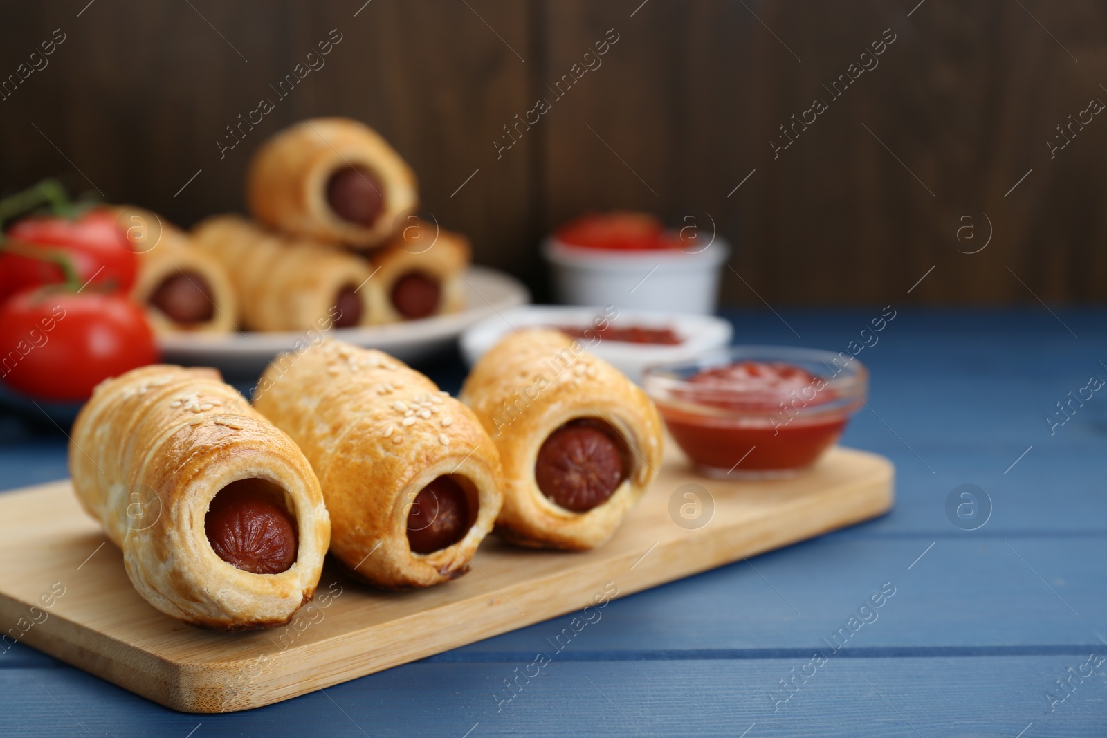 Photo of Delicious sausage rolls and ingredients on blue wooden table, closeup. Space for text