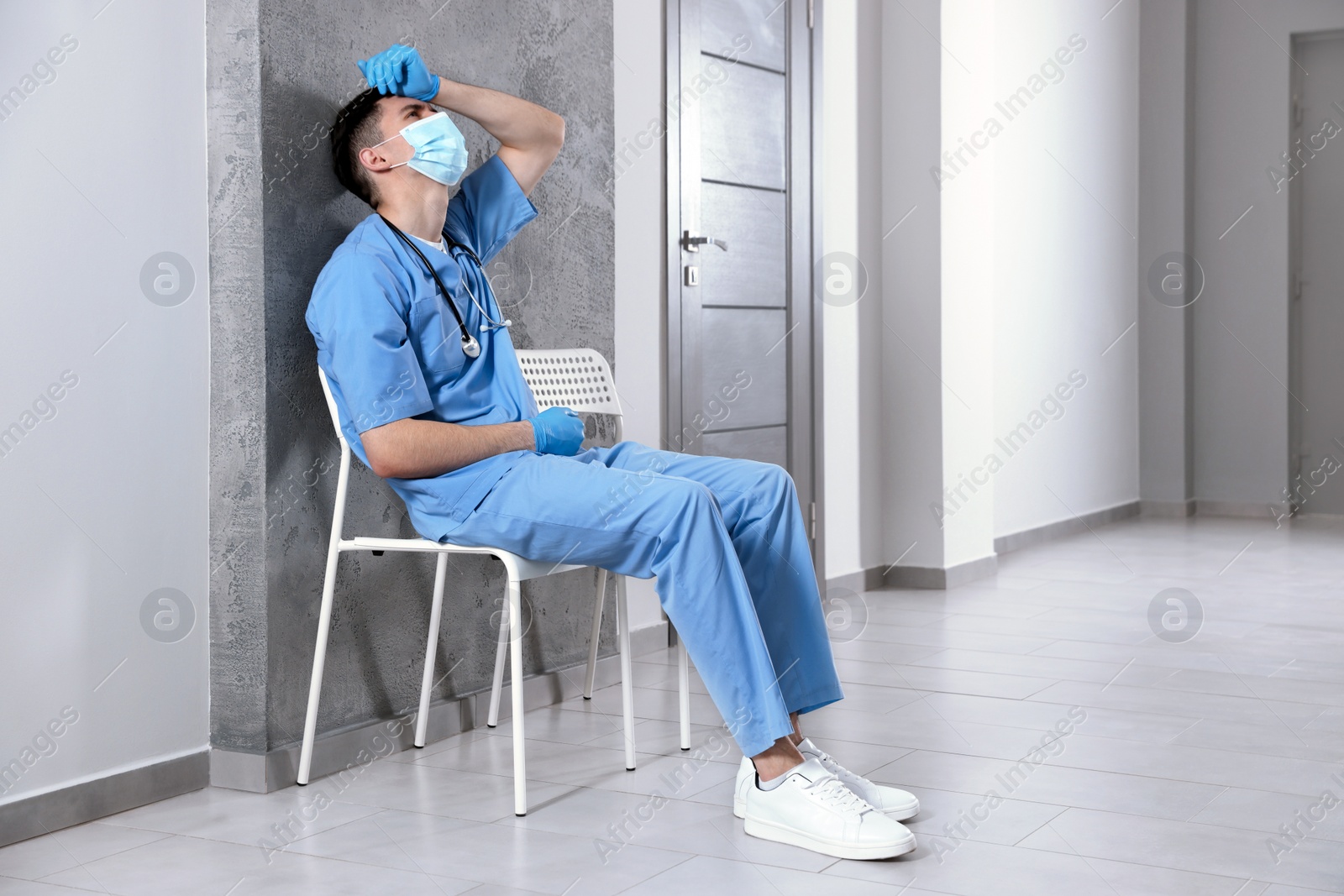 Photo of Exhausted doctor sitting on chair in hospital hallway