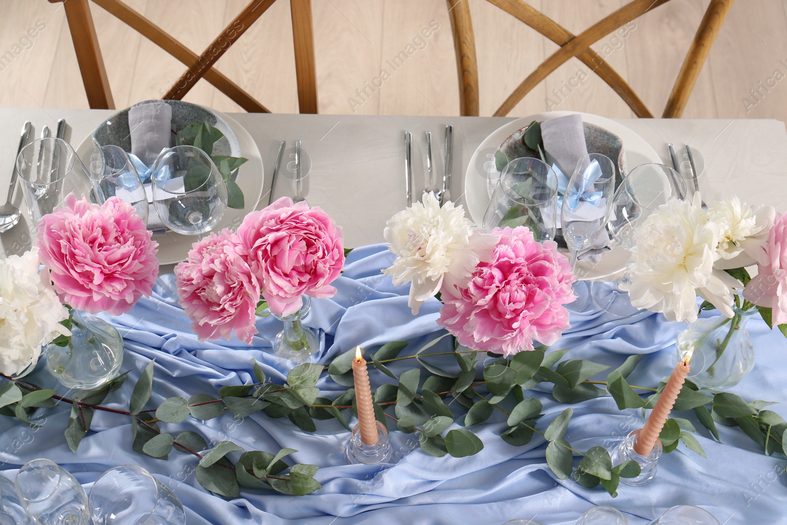 Photo of Beautiful table setting. Peonies, burning candles and branches near plates with greeting cards, napkins and cutlery on table indoors