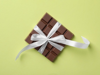 Photo of Tasty milk chocolate bar with ribbon on yellow background, top view