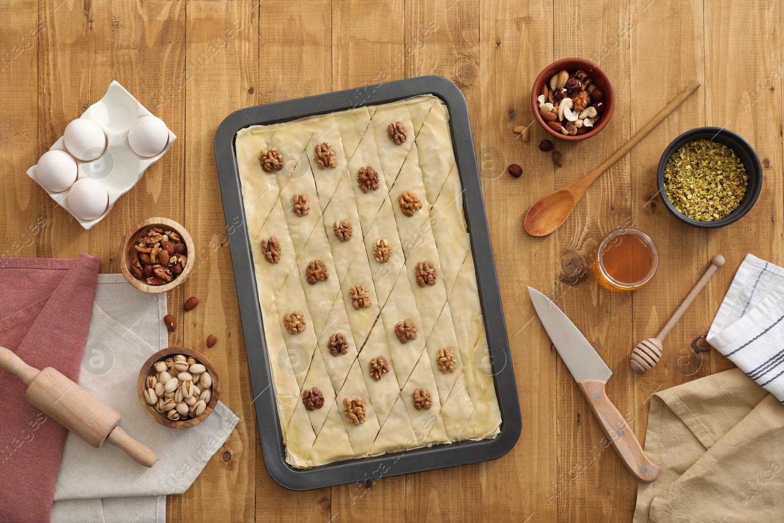 Photo of Making delicious baklava. Baking pan with dough and ingredients on wooden table, flat lay