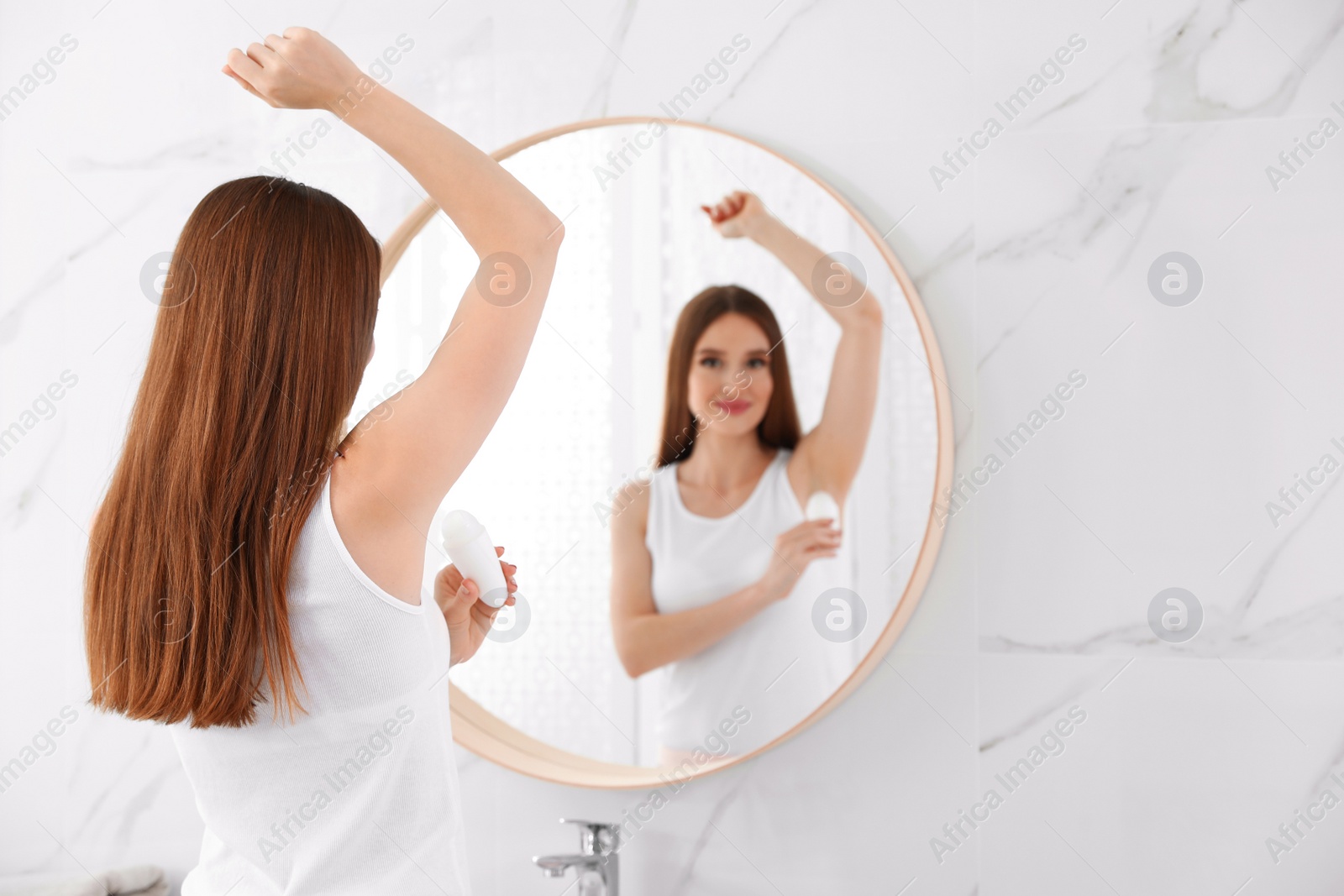 Photo of Beautiful young woman applying deodorant in bathroom. Space for text