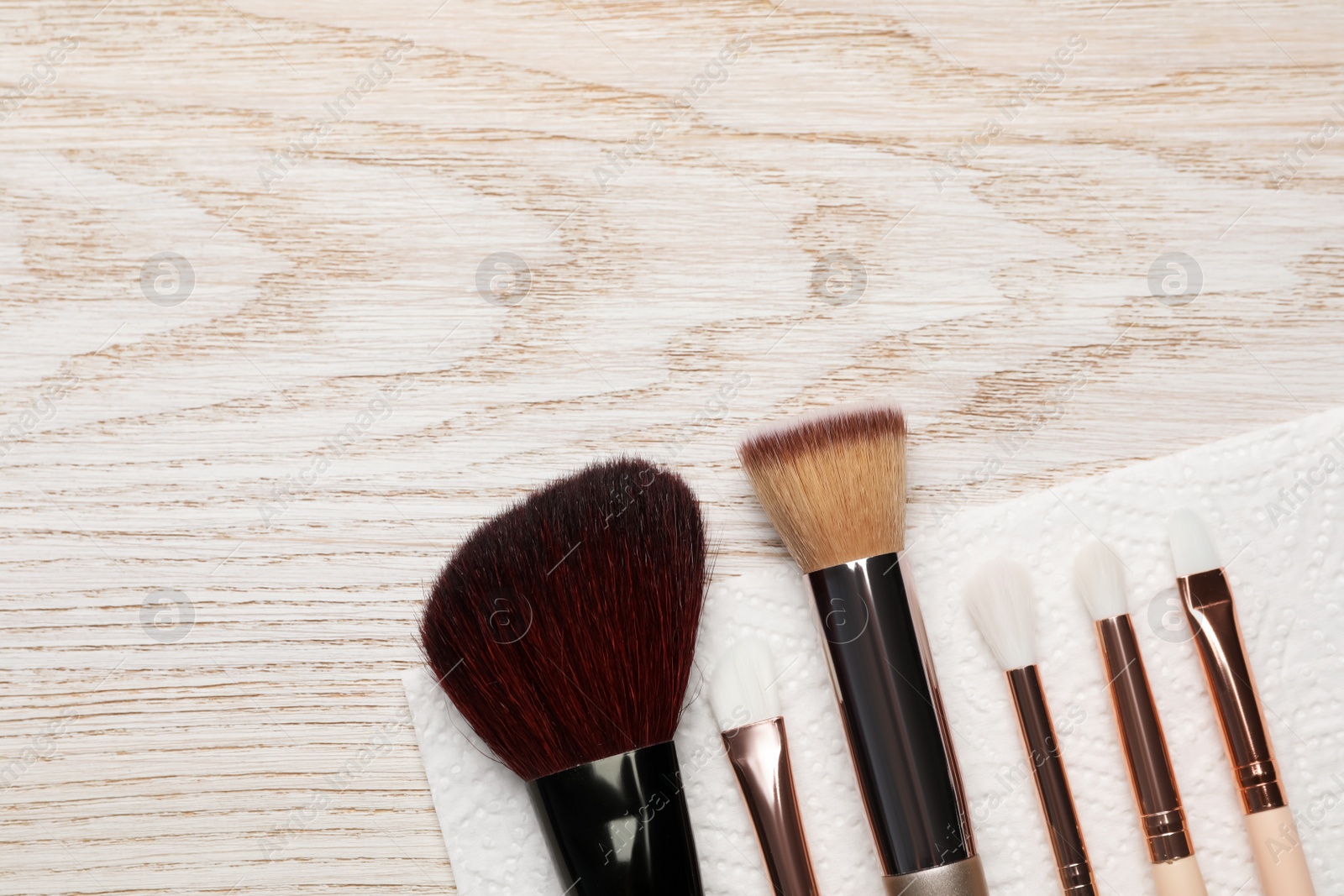 Photo of Clean makeup brushes with napkin on wooden table, flat lay. Space for text