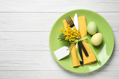 Festive Easter table setting with eggs and floral decor on white wooden background, top view. Space for text