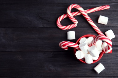 Photo of Cup of tasty cocoa with marshmallows and Christmas candy canes on black wooden table, flat lay. Space for text