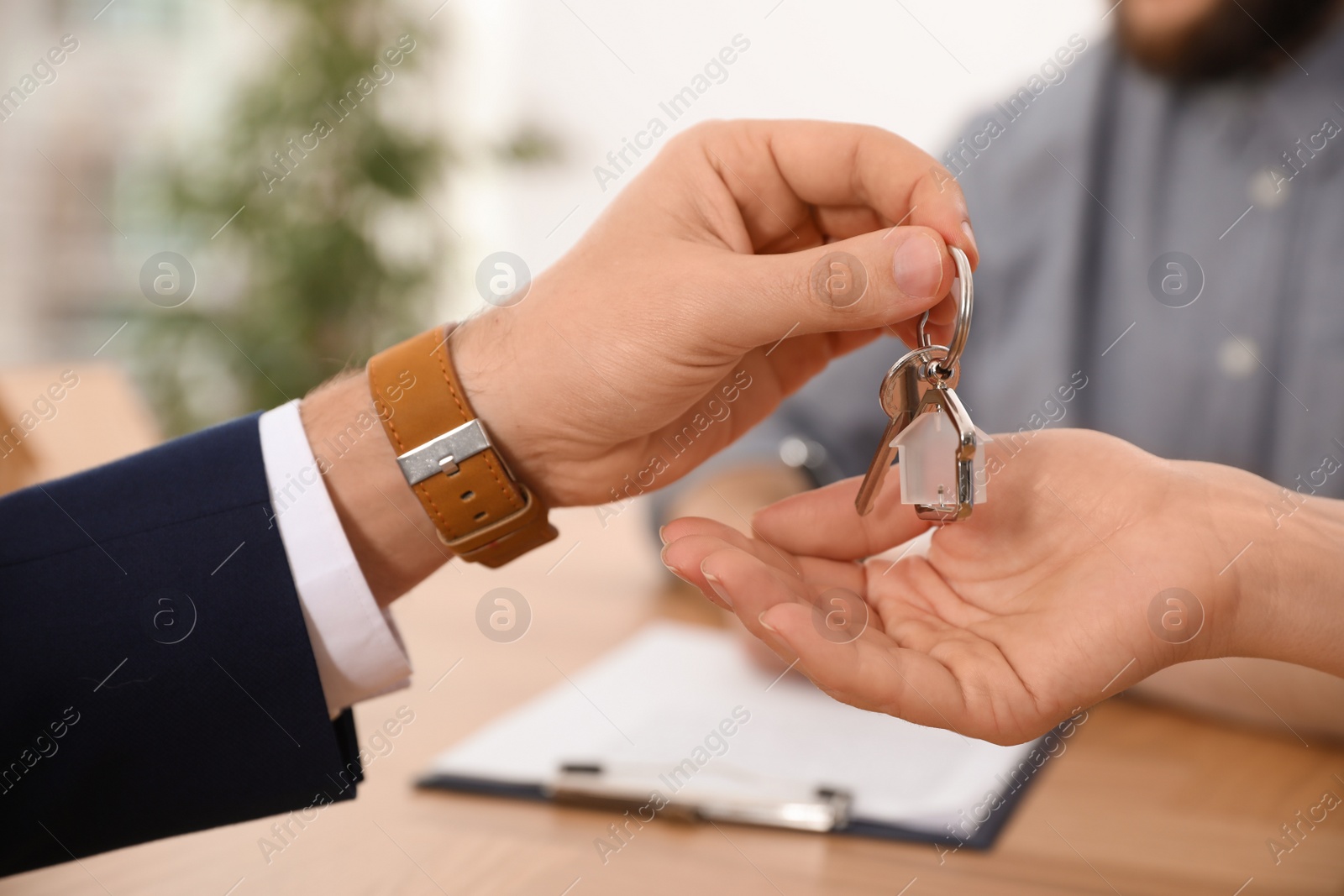 Photo of Real estate agent giving key with trinket to client in office, closeup