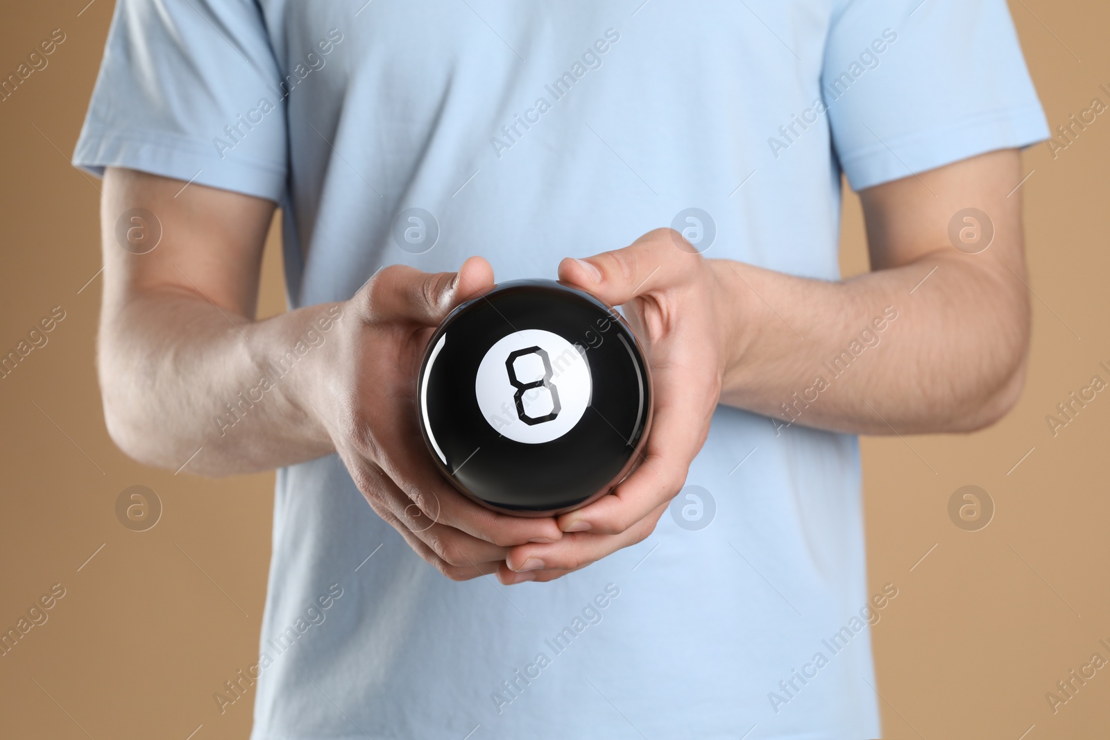 Photo of Man holding magic eight ball on light brown background, closeup