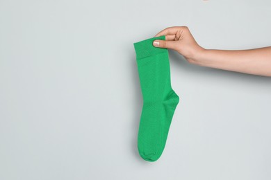 Photo of Woman holding green sock against grey background, closeup