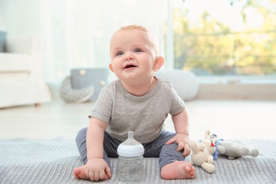 Photo of Cute baby with bottle sitting on floor in room