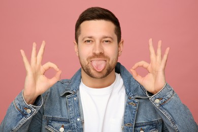 Happy man showing his tongue and OK gesture on pink background