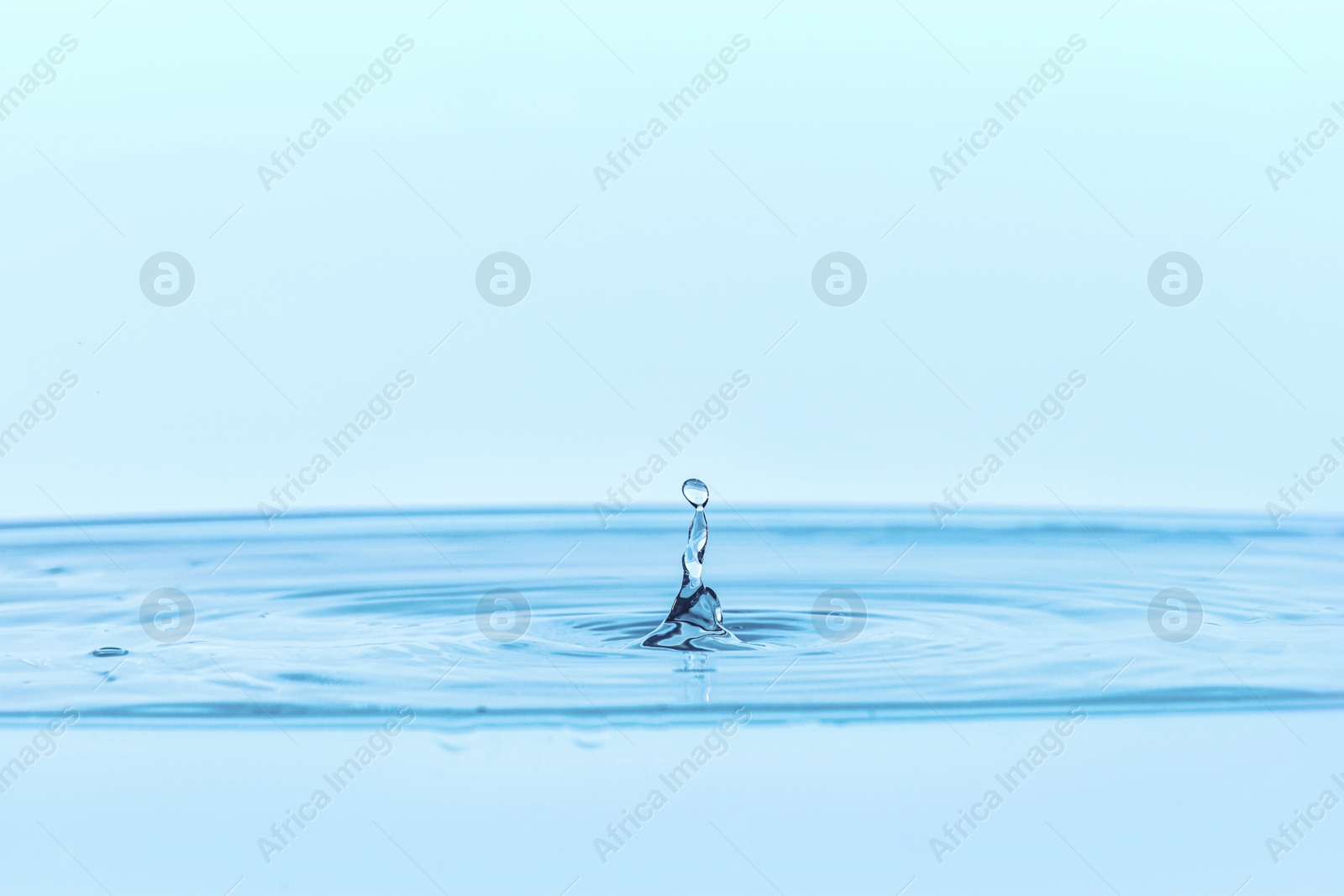 Photo of Splash of clear water with drop on light blue background, closeup