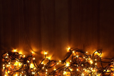 Beautiful bright Christmas lights on wooden background, flat lay. Space for text