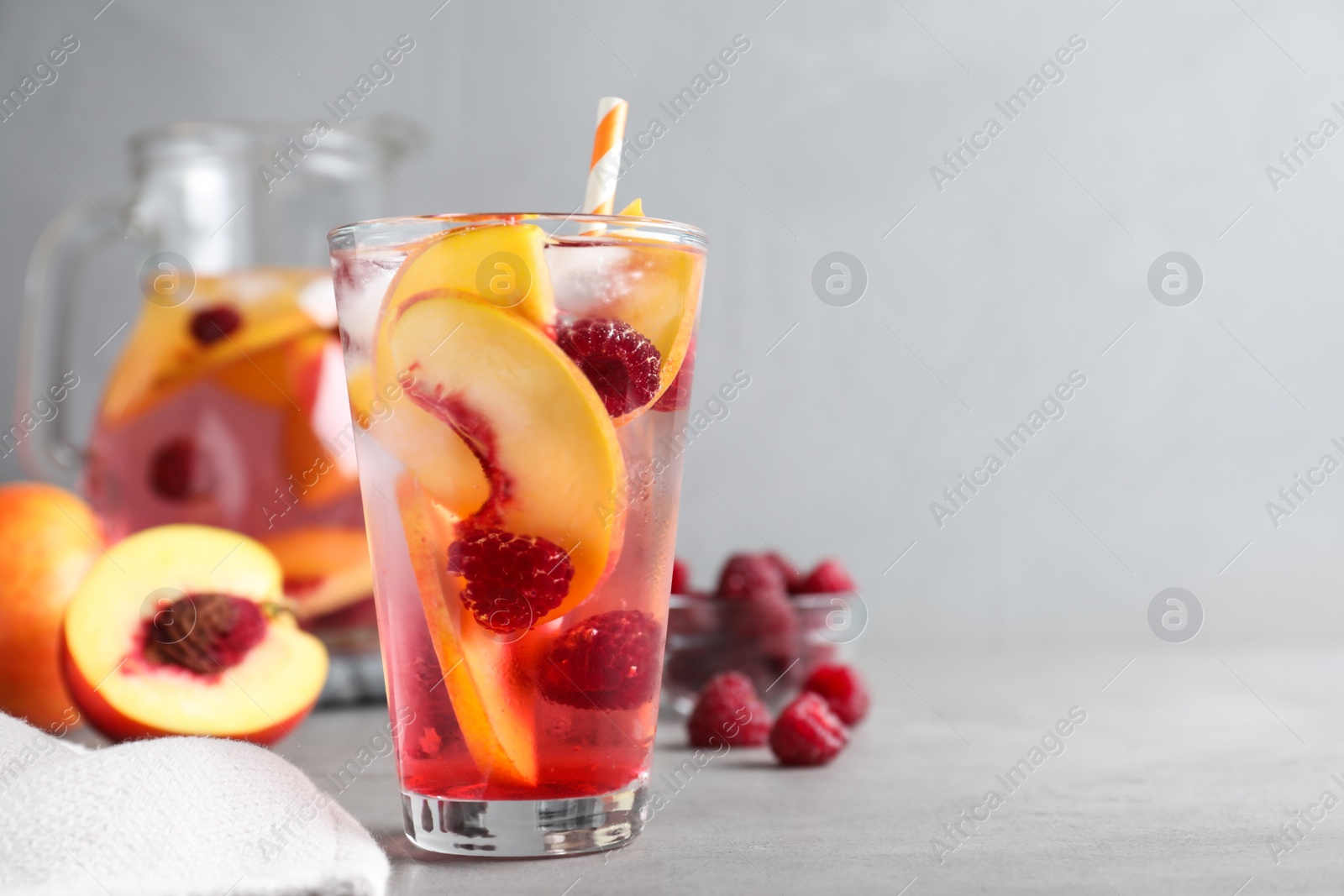 Photo of Delicious peach lemonade with soda water and raspberries on grey table, space for text. Fresh summer cocktail