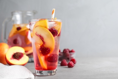 Delicious peach lemonade with soda water and raspberries on grey table, space for text. Fresh summer cocktail