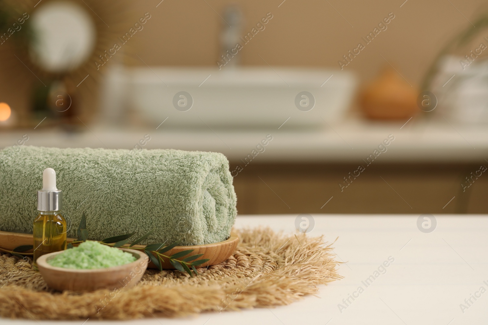 Photo of Spa composition. Rolled towel, cosmetic product, sea salt and twig on table indoors. Space for text