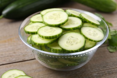 Photo of Cut cucumber in glass bowl on wooden table, closeup