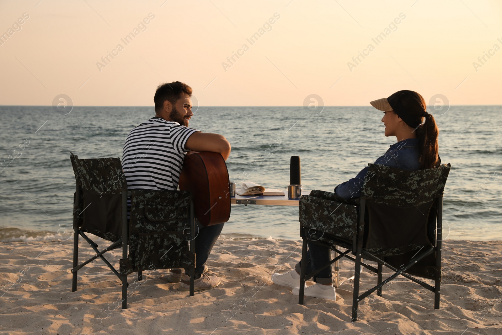 Photo of Young man playing guitar to his beloved girlfriend on beach. Camping season